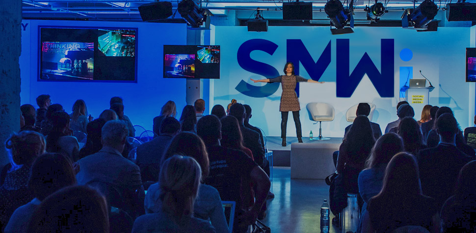 Speaker on stage in front of the SMWi logo at Social Media Week
